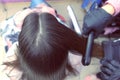 Hairdresser straights dark brown hair of beautiful woman using hair tongs in beauty salon. Back view.