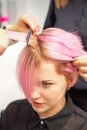 Hairdresser straights pink hair of woman by hair iron