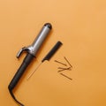 Hairdresser tools: curling iron, rat tail comb, bobby pins over orange. Top view