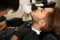 Hairdresser trimming client`s beard in barbershop