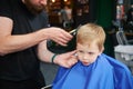 Hairdresser using electric shaver to cut boy's hair. Little kid getting first haircut in barbershop. Royalty Free Stock Photo