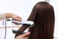 Hairdresser using modern flat iron to style client`s hair