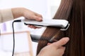 Hairdresser using modern flat iron to style client`s hair in salon