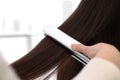 Hairdresser using modern flat iron to style client`s hair in salon