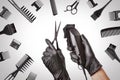 Hairdressers hands in black rubber gloves holds hair clipper and scissors surrounded by professional hairdressing accessories