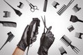 Hairdressers hands in black rubber gloves holds hair clipper and scissors surrounded by professional hairdressing accessories