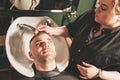 Hairdressing, girl hairdresser washes the head of a young guy in a barbershop