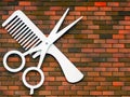 Hairdressing: scissors and comb emblem hanging on a brick wall