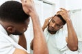 Young african man checking for thinning hair in mirror at bathroom Royalty Free Stock Photo