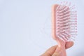 Hair loss problems with hand holding a pink hairbrush on white background. Falling black hair clinging to the comb