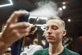 Hairstyling. Barber or hairdresser fixing new modern haircut with hairspray of young guy sitting in barber shop chair Royalty Free Stock Photo