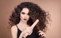 Hairstyling. Curly Beauty hair. Glamour portrait of beautiful woman model holding straightening iron. Brunette with marsala matte Royalty Free Stock Photo