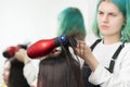 Hairstylist drying brunette hair with red hair dryer, blue hairbrush in beauty salon