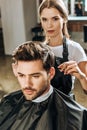 Hairstylist looking at camera while cutting hair to handsome young man Royalty Free Stock Photo