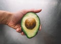 Half an avocado in a hand on the background of a steel table top view horizontal, fresh healthy food breakfast on kitchen, green
