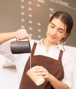 Half-body angle of beautiful caucasian barista women fills white milk into takeaway hot coffee cup at coffee bar in cafe coffee