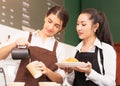 Half-body angle of caucasian and Asian barista women preparing takeaway hot coffee and bread for customer with menu background in