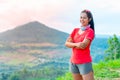 Half-body photo of a female trail runner wearing pink runner, sportswear, smiling, looking at the camera. on the gravel ground on