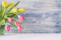 Half bouquet red and yellow tulips in green glass vase on blue shabby wooden background with copy space. Spring easter home decor. Royalty Free Stock Photo