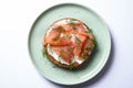 Half a bun, oiled with fresh cream, garnished with smoked fish and sprinkled with fresh dill and sesame seeds on a green plate