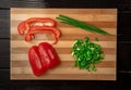 Half and chopped pieces of red sweet pepper, stalks and cutting green onions in water drops on wooden board. Sliced bell Royalty Free Stock Photo