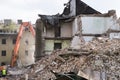 Half collapsed brick house covered in dust and debris with a crasher machine