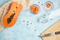 Half of colorful orange papaya on kitchen table with knife, cutting board and bottle of soda water