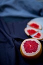 Half cut grapefruit and pieces of fruits in a white plate on the kitchen towels cloth rags blue grey dark hue close-up of