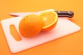 Half cut orange on chopping board with knife