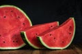 Half of a cut ripe watermelon with two large slices and red juicy pulp on a wooden table against a dark background of black Royalty Free Stock Photo