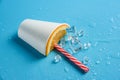 Half of a disposable glass with an orange slice and a cocktail tube on a blue background with ice cubes Royalty Free Stock Photo