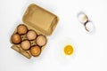 Half a dozen egg container and one raw broken egg on white surface showing yellow yolk