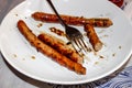 Half-eaten barbecue sausages from the grill lie with a fork on a plate Royalty Free Stock Photo