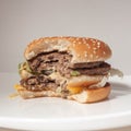 Half-eaten Burger with two cutlets on a white plate and a light background, side view Royalty Free Stock Photo