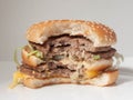 Half-eaten Burger with two cutlets on a white plate and a light background, side view Royalty Free Stock Photo