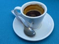 Half empty full white porcelain coffee cup, saucer and a tea spoon on blue background. Royalty Free Stock Photo