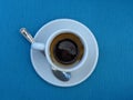 Half empty full white porcelain coffee cup, saucer and a tea spoon on blue background. Top view.