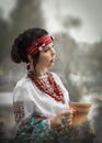 A half-face portrait of a pretty young female dressed in a Ukrainian folk costume holding a clay jug outside. Cosplay