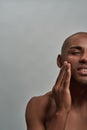Half face portrait of shirtless young african american man applying lotion on his face, posing isolated over gray Royalty Free Stock Photo