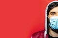 Half face portrait of young hooded guy, wearing medical flu mask on face against coronavirus. Studio background of red color. Royalty Free Stock Photo