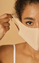 Half face portrait of young mixed race woman adjusting her facial mask, looking at camera, posing over beige background Royalty Free Stock Photo