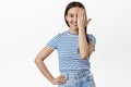 Half face. Portrait of young 20s girl covering one eye and smiling at camera, standing in casual striped t-shirt Royalty Free Stock Photo