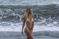 Half face shot of cute young woman in gold bikini on background of stormy ocean