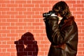 Profile of a young photogropher shooting wih camera against brick wall