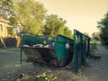Half filled trash dumpster in ghetto neigborhood with some litter about