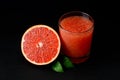 Half of fresh ripe grapefruit and glass of freshly squeezed grapefruit juice with pulp on black background. Low key image.