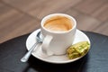 Half full cup of espresso macchiato with metal spoon and half eaten pistachio macaron on saucer. Black leather table