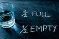 Half-full or half-empty glass of water, with text written on a blackboard, showing optimism or pessimism, concept Royalty Free Stock Photo