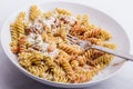 A half full white plate, with fusilli, covered with tomato sauce