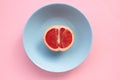 Half of grapefruit on a blue plate on a pink background. Top view, copy space. Royalty Free Stock Photo